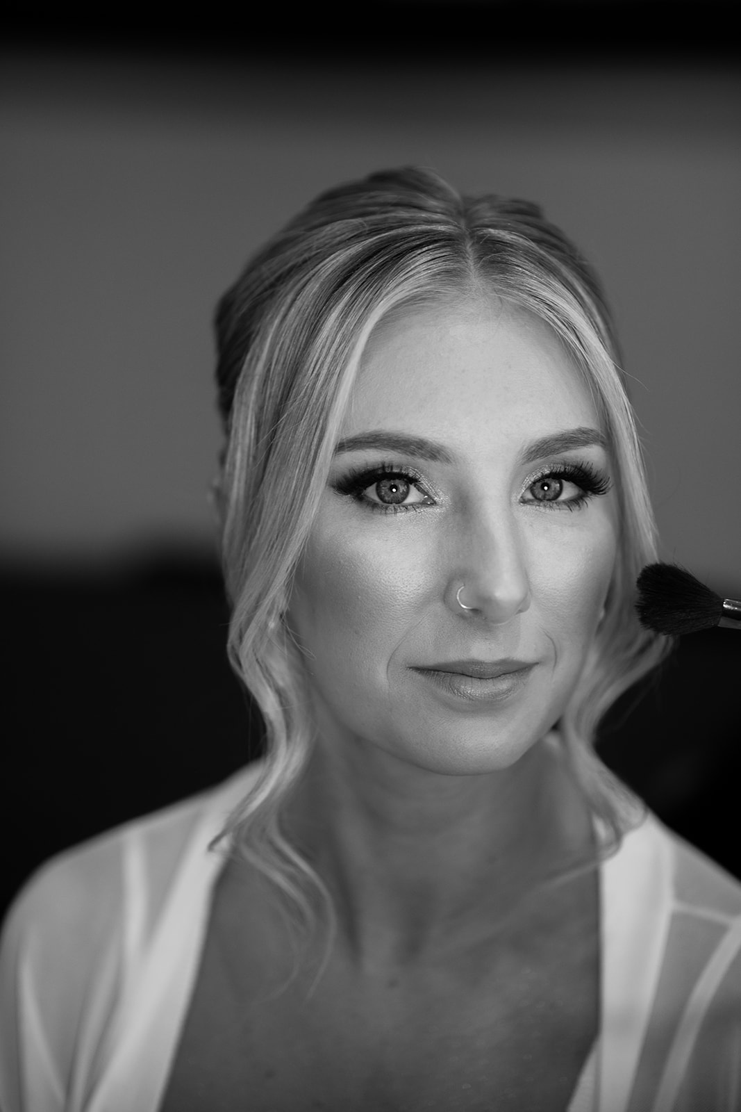 Black and white close-up of a bride looking serene while having her makeup applied during wedding prep.